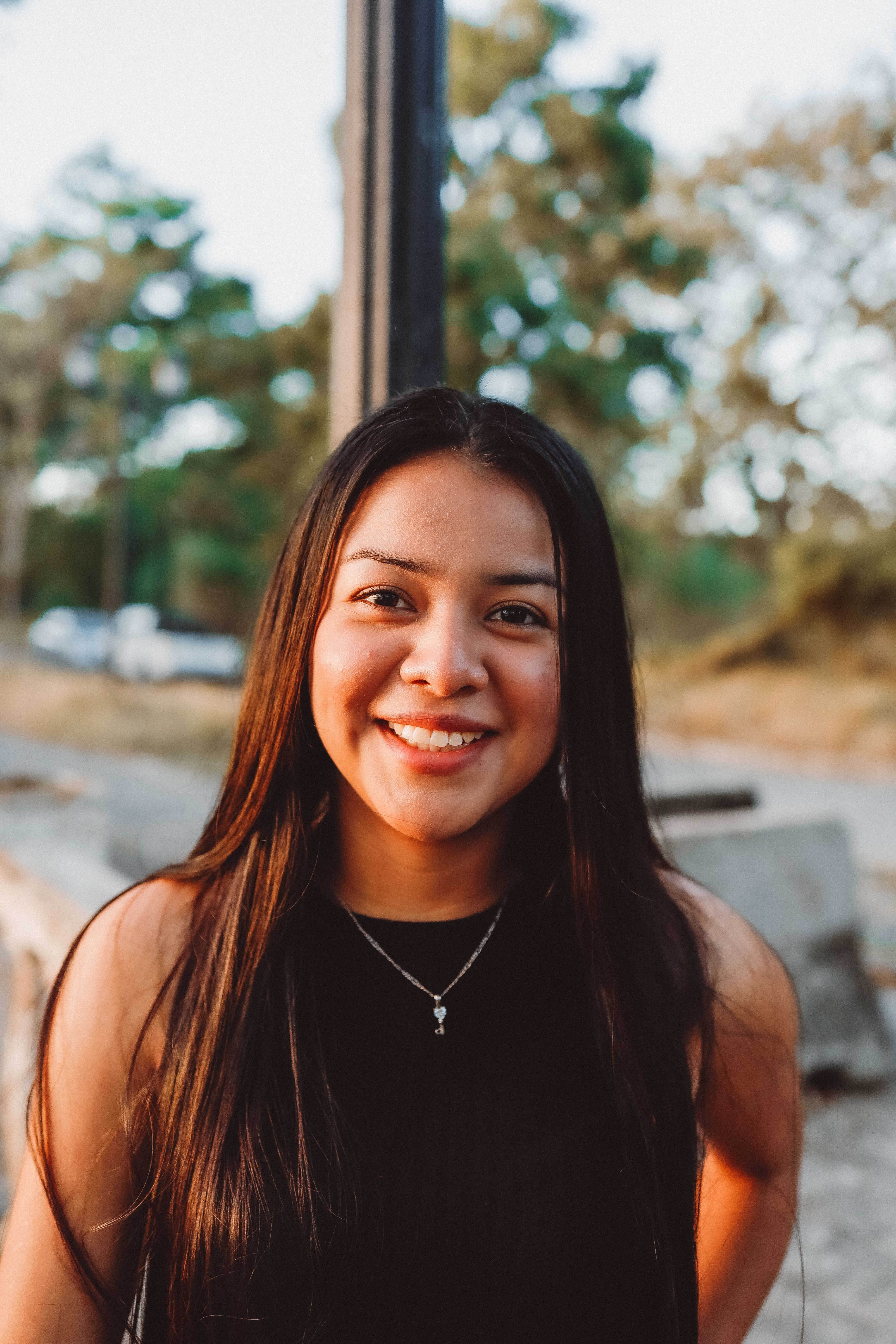 Portrait of a smiling woman outdoors with trees in the background, captured during the day.