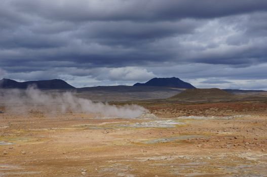 Dramatic Icelandic landscape showcasing geothermal steam and cloudy skies.