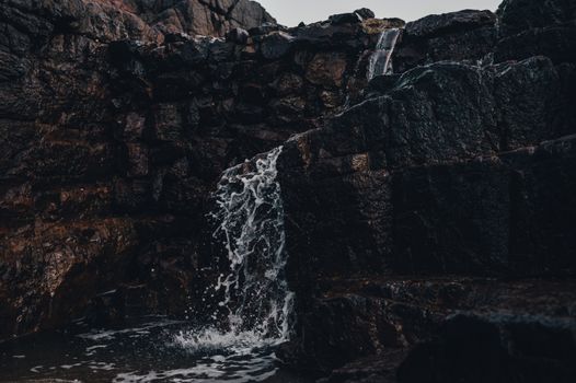 A close-up of a cascading waterfall over dark geological rock formations.
