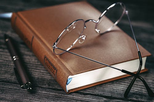 Silver Framed Eyeglasses on Brown Book