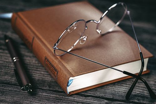 Free A brown hardcover book with eyeglasses and a pen on a wooden table. Stock Photo