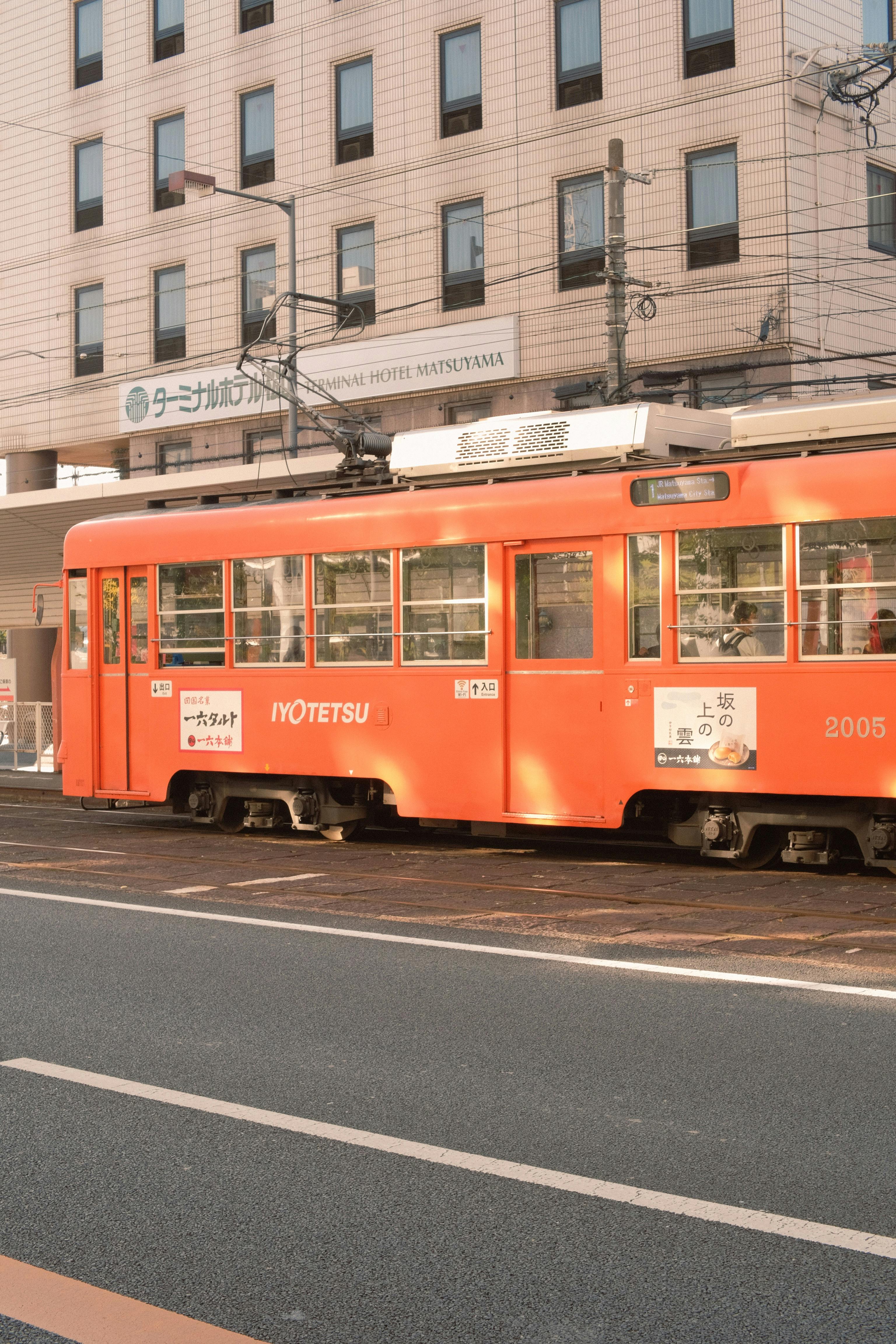 Free A bright orange tram on the tracks near a city hotel, showcasing urban transport. Stock Photo