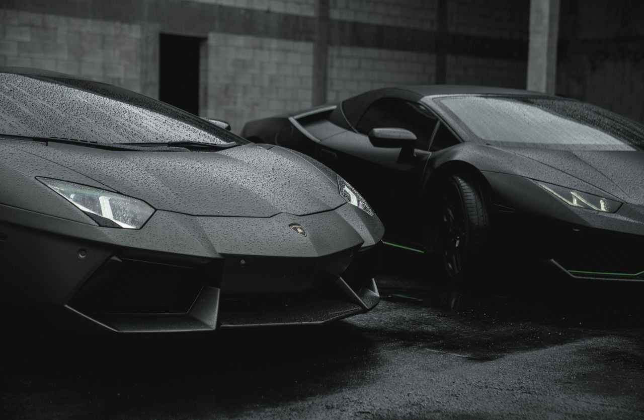 two sleek black luxury sports cars on a rainy day outdoors showcasing
