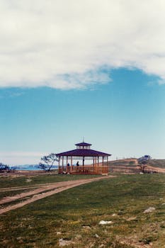 A serene wooden pavilion sits on a grassy field under a cloudy sky, evoking tranquility.