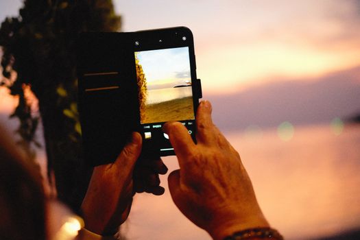 A person photographing a serene sunset on a beach using a smartphone, highlighting travel and technology.