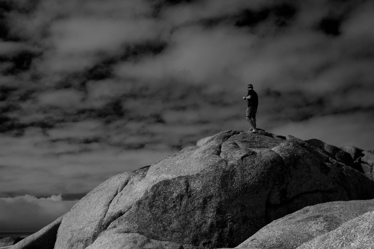 silhouette of a man standing on a rocky peak under a moody sky