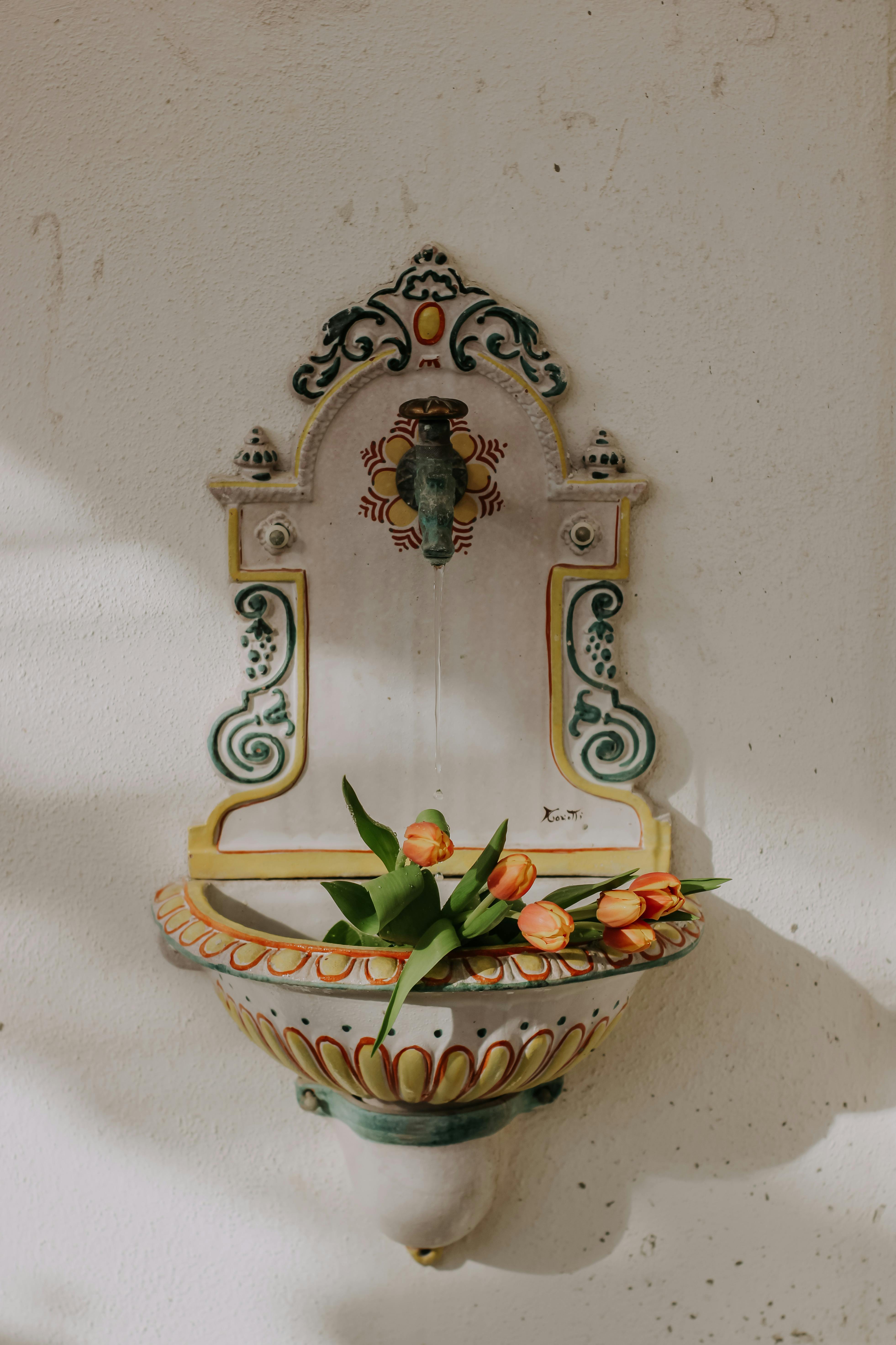 Decorative wall fountain with intricate designs and fresh flowers, indoor setting.