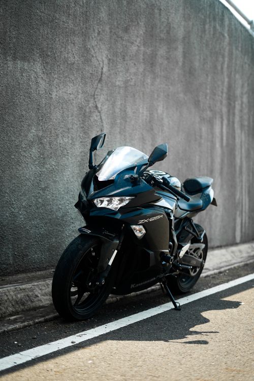 Free A modern black sports motorcycle parked on a sunny urban street against a concrete wall. Stock Photo
