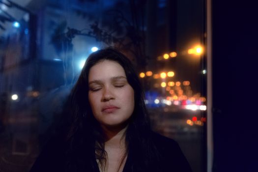 A serene woman with closed eyes reflects in a cityscape background at night.