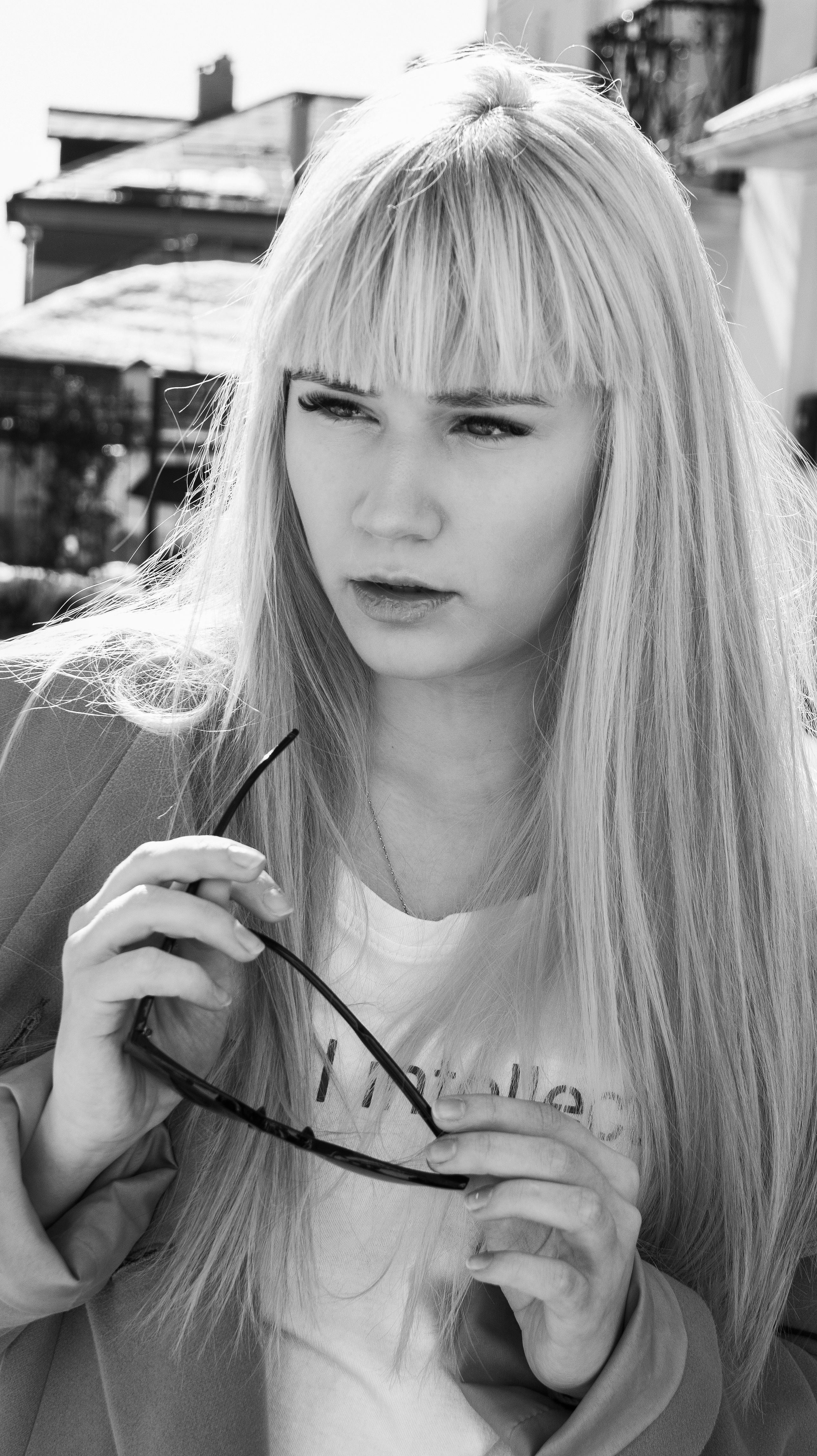 Stylish black and white portrait of a blonde woman holding sunglasses on a sunny day.