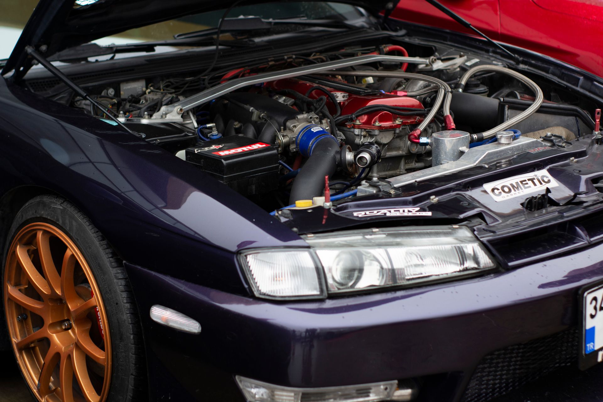 Close-up of a purple car engine featuring custom modifications and orange alloy wheels.