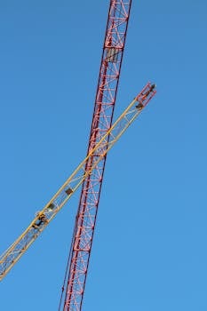 Vibrant construction cranes crossing an azure sky on a clear day.