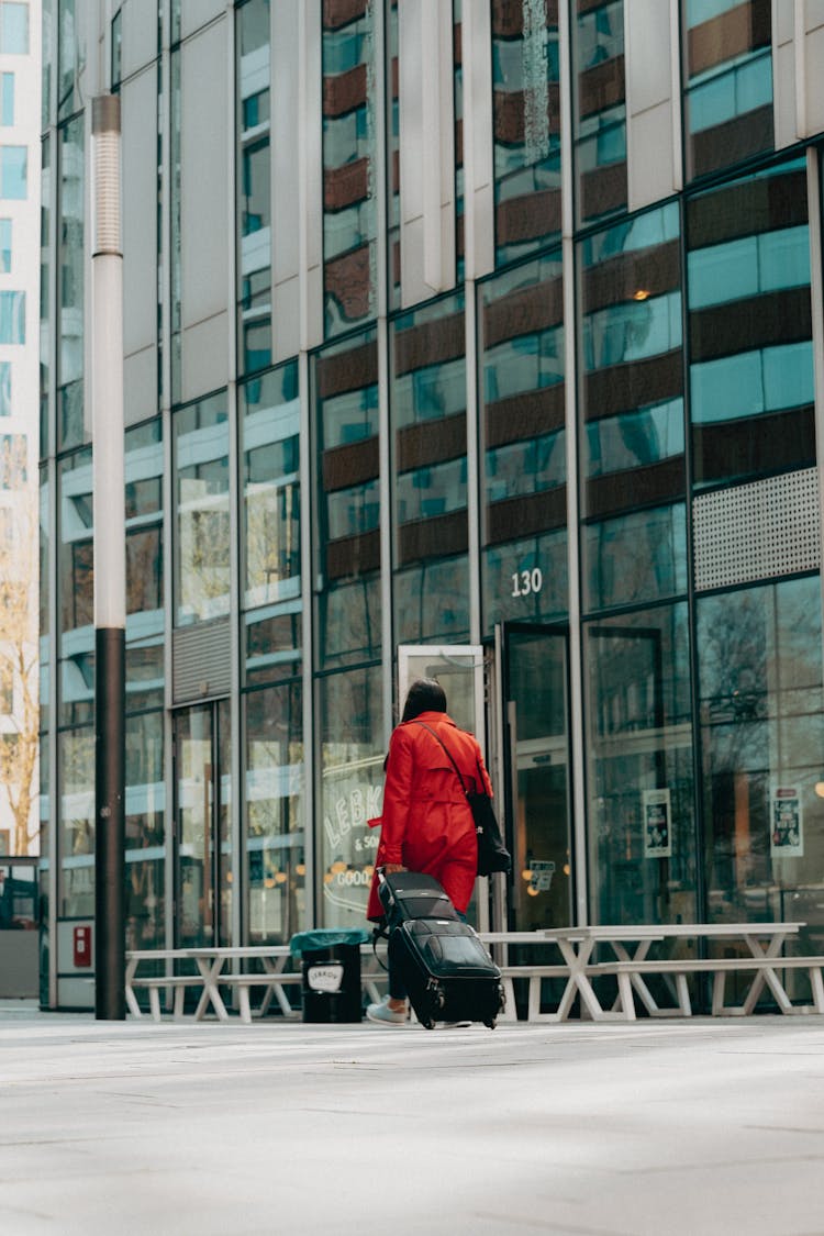 Back View Of A Person Wearing A Red Coat Walking With A Suitcase