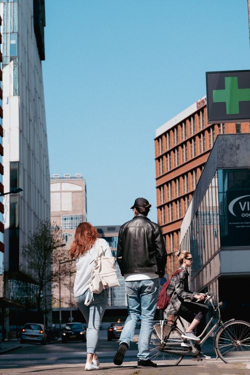 Free A city street scene featuring pedestrians and a cyclist with modern buildings in the background. Stock Photo