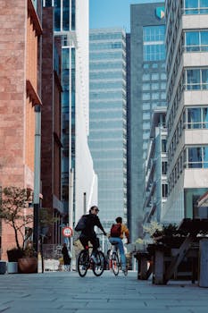 Two cyclists enjoying a ride through a modern cityscape flanked by towering skyscrapers.