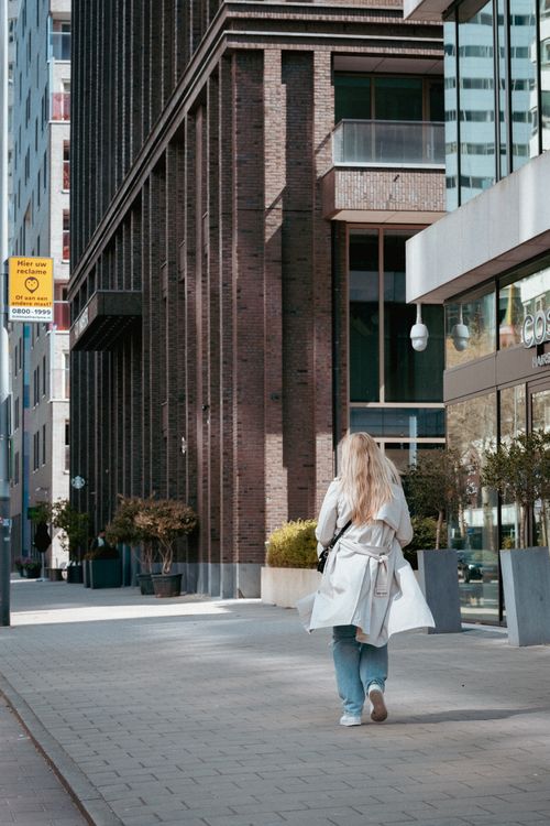 Free Woman in trench coat walking along an urban sidewalk, capturing street life. Stock Photo