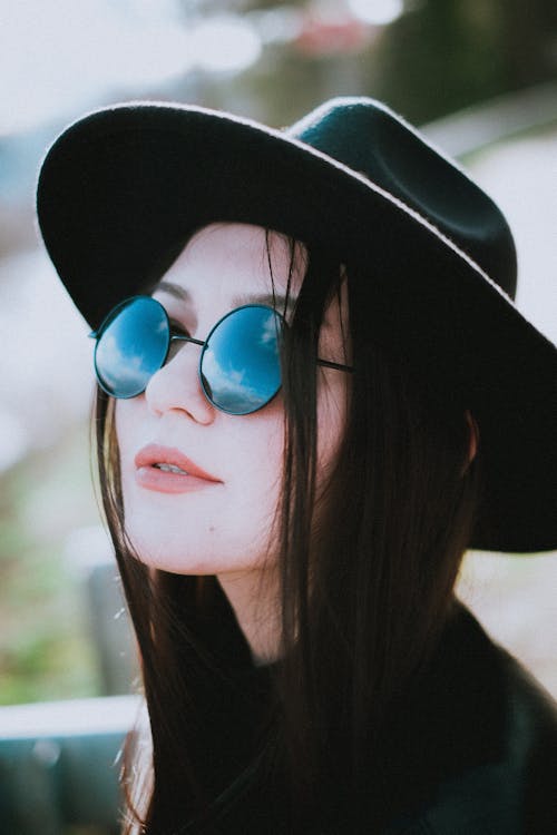 A Woman Wearing Black Sun Hat and Black Sunglasses with Reflections of Clouds