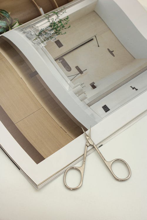A Magazine and Stainless Scissors on White Surface