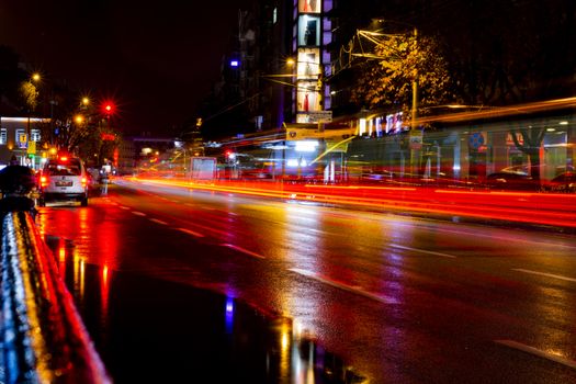 Dynamic city street at night with vibrant light trails and reflections on wet pavement.