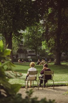 Two people enjoy a sunny day in a vibrant city park surrounded by trees.