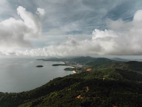 Free Stunning aerial view of Phuket's lush hills and coastline under a cloudy sky. Stock Photo