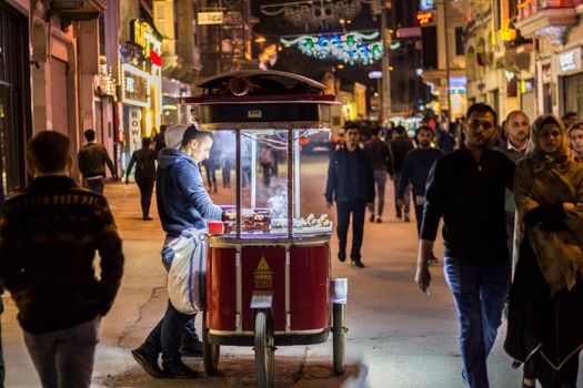 A bustling night market scene with a street vendor selling food under bright lights.