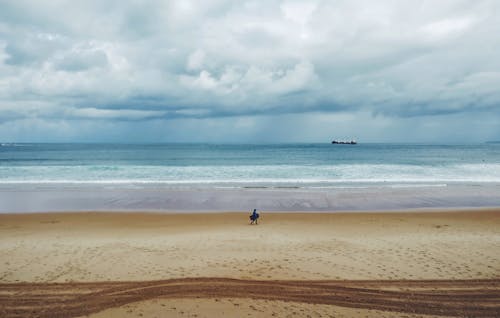 Person Walking on Sand Near Body of Water