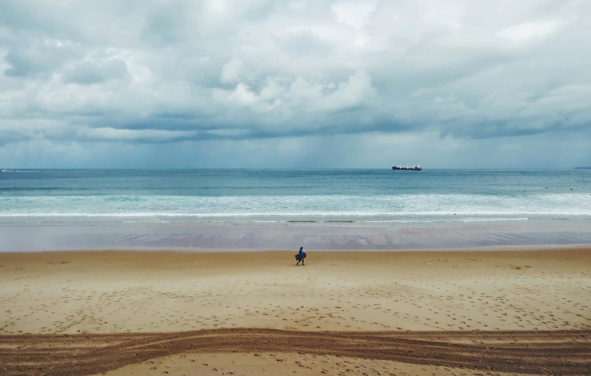 A scenic view of Santander beach showing a lone surfer under cloudy skies.