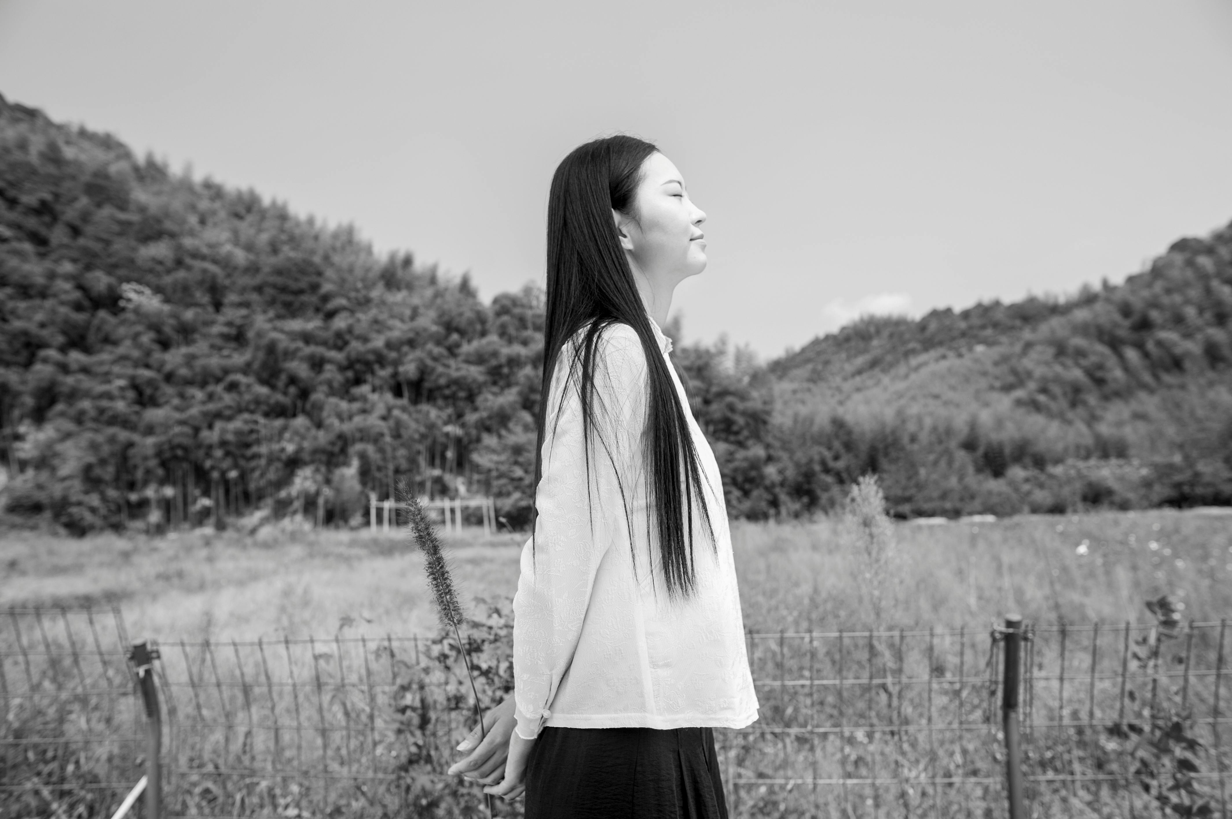 Black and white portrait of a woman with eyes closed, standing in a serene field.