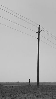 Black and white landscape featuring a power pole and a distant figure. Minimalist and serene setting.