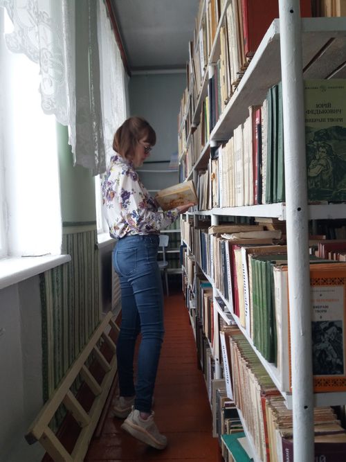 Free A woman browses books in a well-lit library aisle with rows of bookshelves. Stock Photo
