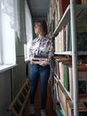 Woman in Blue Denim Jeans Standing Beside Brown Wooden Bookshelf