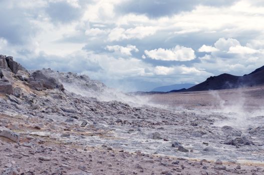 A captivating view of Iceland's geothermal landscape with steam rising amid rugged terrain under a cloudy sky.