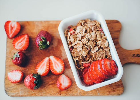 Delicious granola served with fresh strawberries on a wooden chopping board.