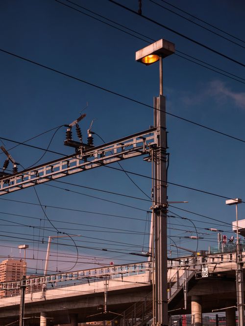 Free A street light stands tall among urban infrastructure under a blue sky, showcasing modern city dynamics. Stock Photo