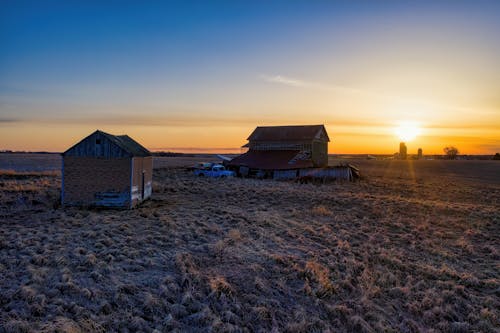 Wooden House and Barn on Brown Field during Sunset