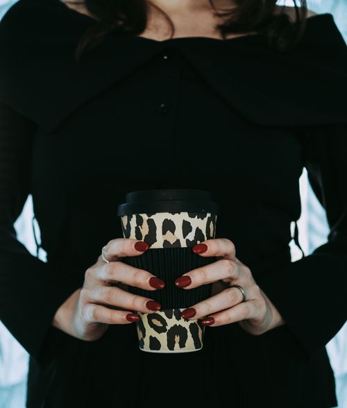 Free Close-up of a woman holding a leopard print coffee cup with red nails, emphasizing style and warmth. Stock Photo