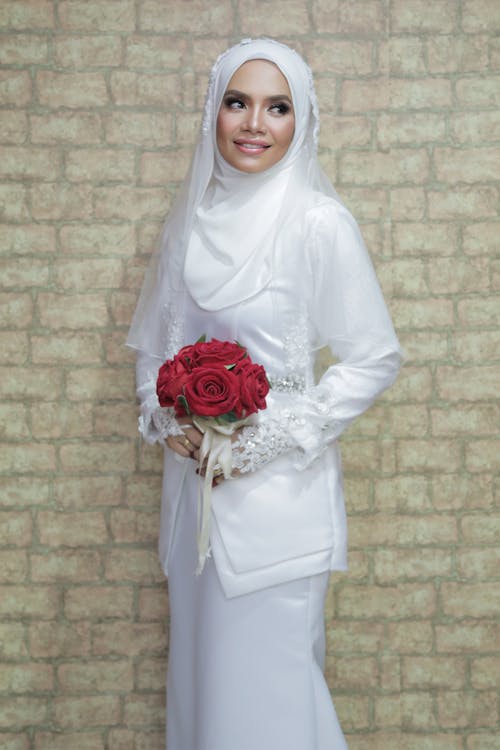 Woman in White Clothes Holding a Bouquet of Flowers