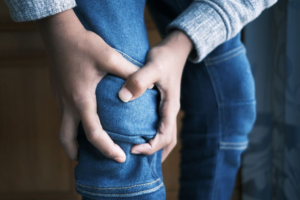 Close-up of a person holding a painful knee before gait analysis and a custom orthotics assessment