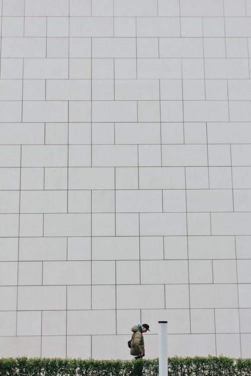 Free A person walks by a vast white tiled wall in Warsaw, Poland, showcasing minimalist urban architecture. Stock Photo