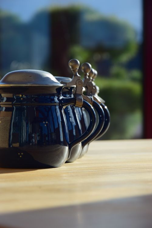 Free Close-up of blue ceramic kettles lined up on a sunlit wooden table in Stuttgart, Germany. Stock Photo