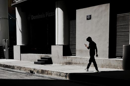 A man in silhouette walks past a city building, capturing urban daily life.