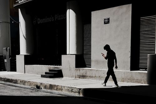 Free A man in silhouette walks past a city building, capturing urban daily life. Stock Photo