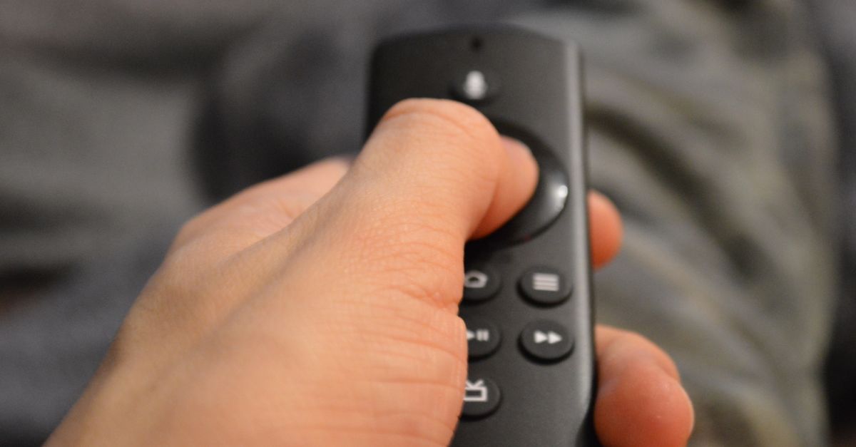 Person relaxing on couch with remote control, watching TV show on a rainy day