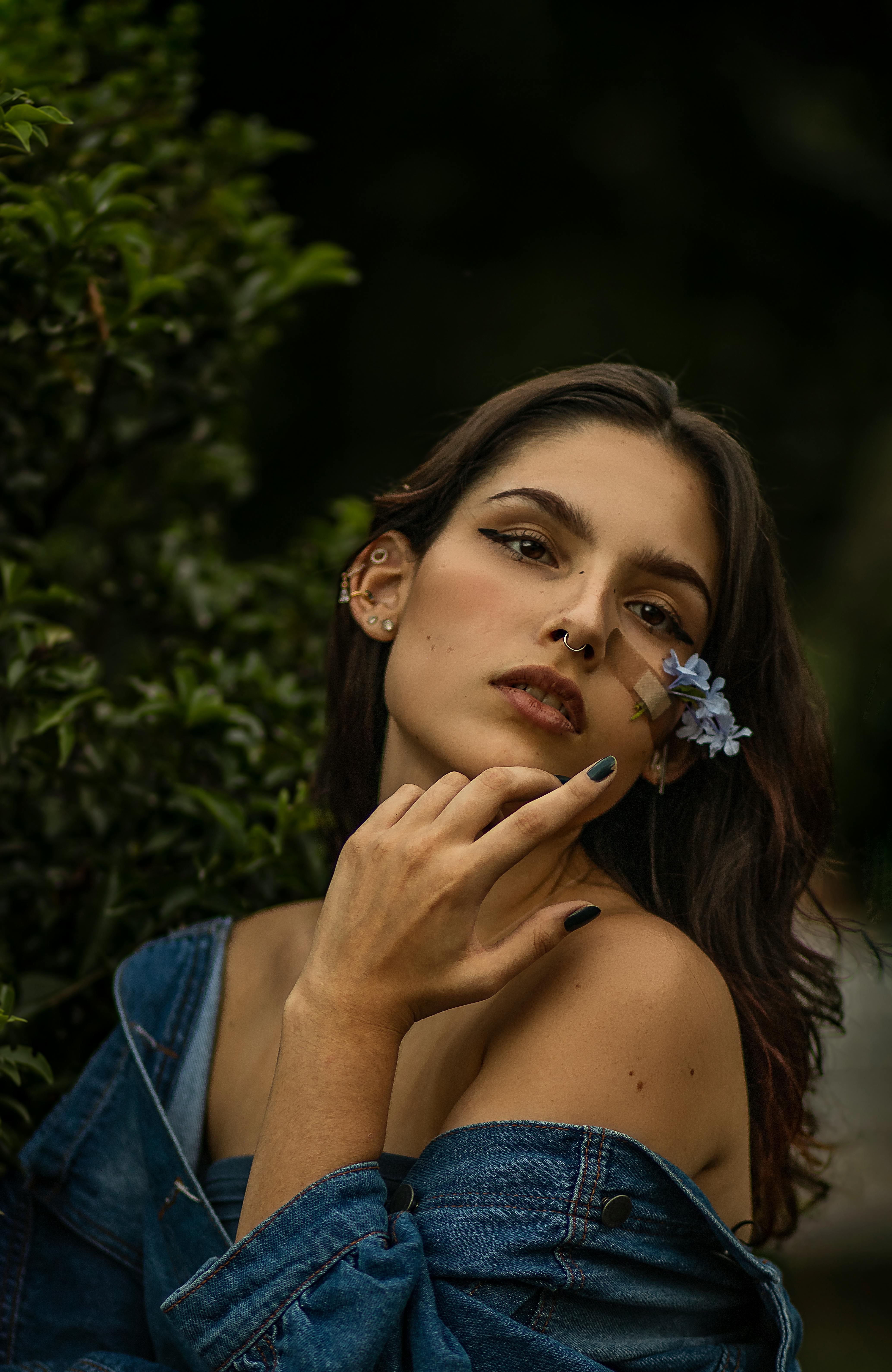 Elegant portrait of a woman with a nose piercing holding a flower outdoors.