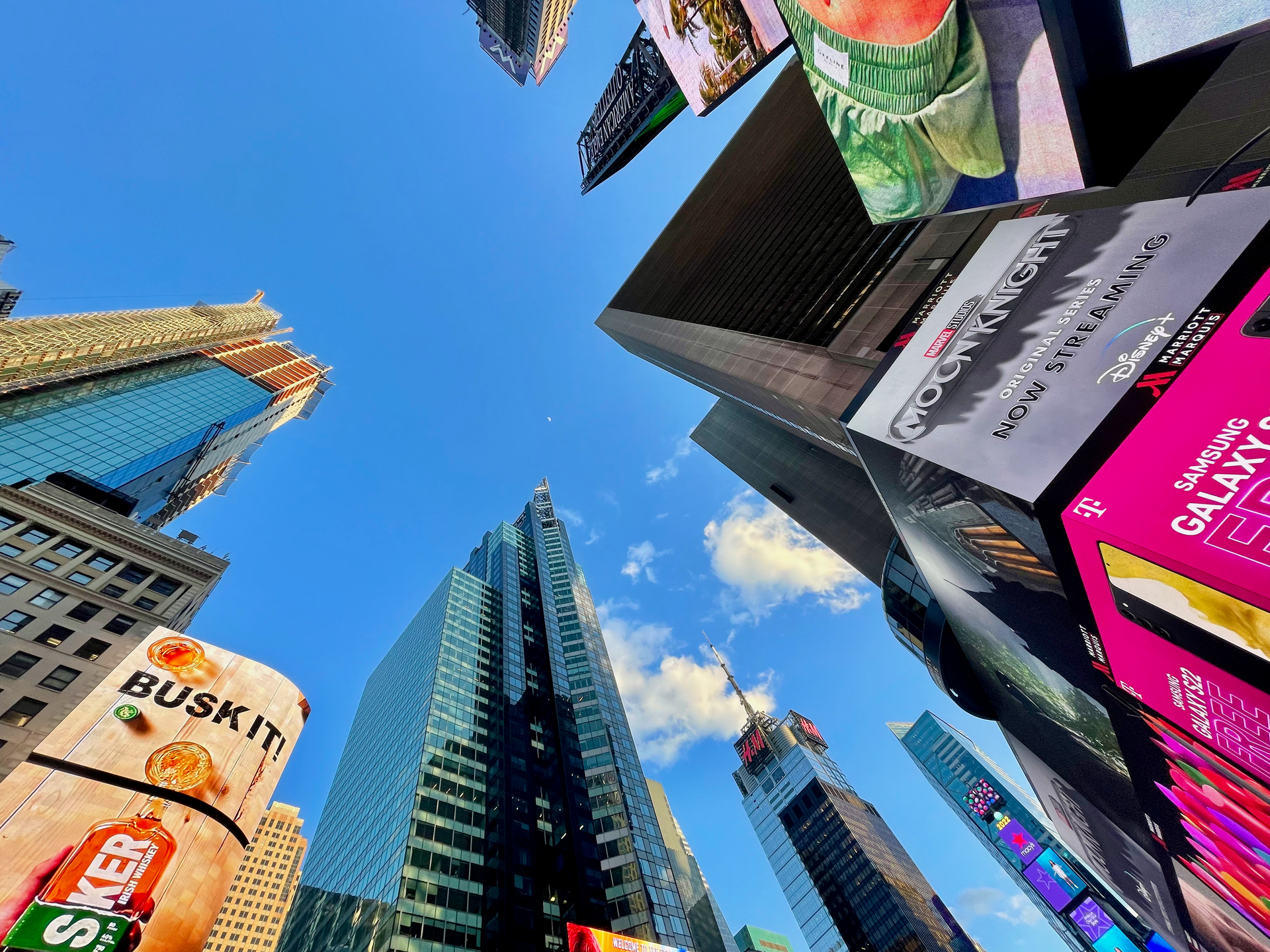 Vibrant view of skyscrapers and billboards under a clear blue sky in Times Square, New York City.