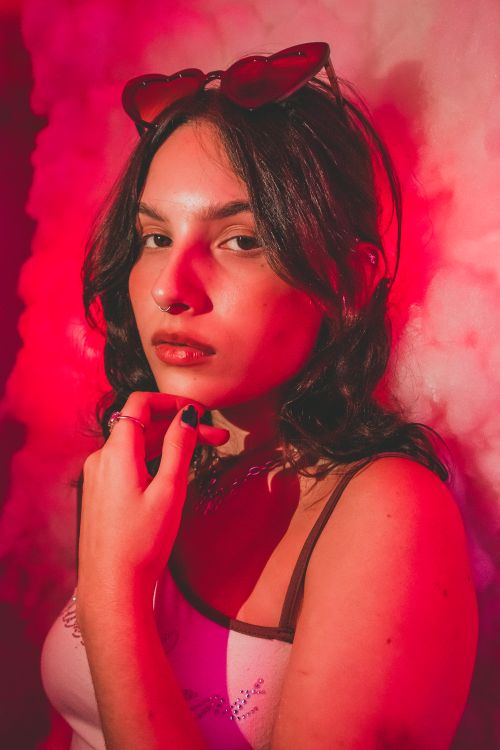 Free Moody portrait of a woman illuminated by red light, wearing sunglasses indoors. Stock Photo
