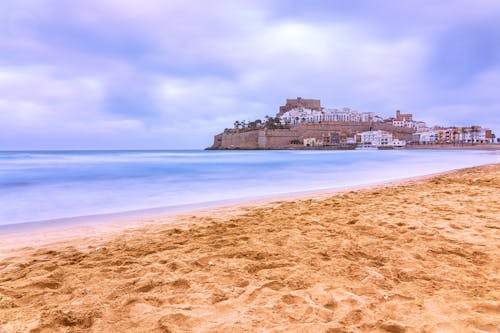 Brown Sand Beach Near City Buildings Under Blue Sky