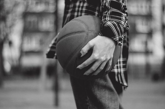 A monochrome image capturing a close-up of a hand gripping a basketball outdoors.