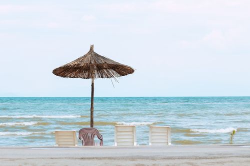 Free Peaceful view of a beach with a straw umbrella and chairs in Pogradec, Albania. Stock Photo